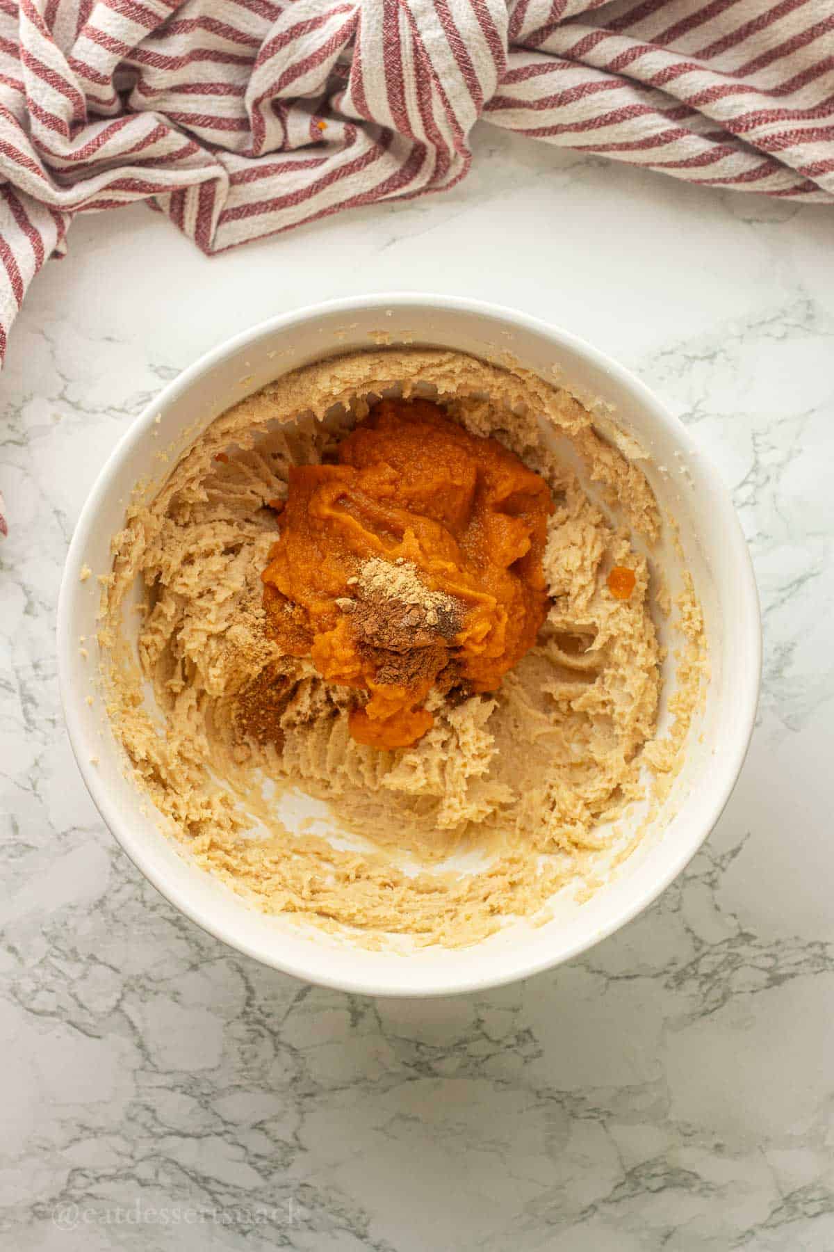Pumpkin puree and pumpkin spice in bowl of creamed butter and sugar.