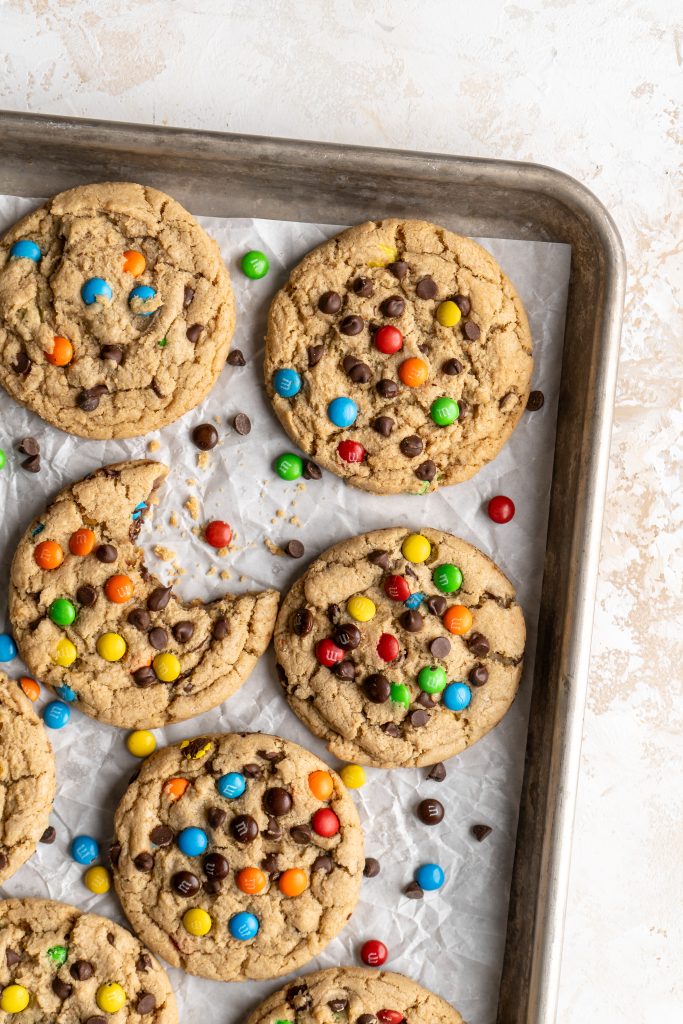 Peanut free monster cookie with bite taken out surrounded by whole cookies on baking sheet.