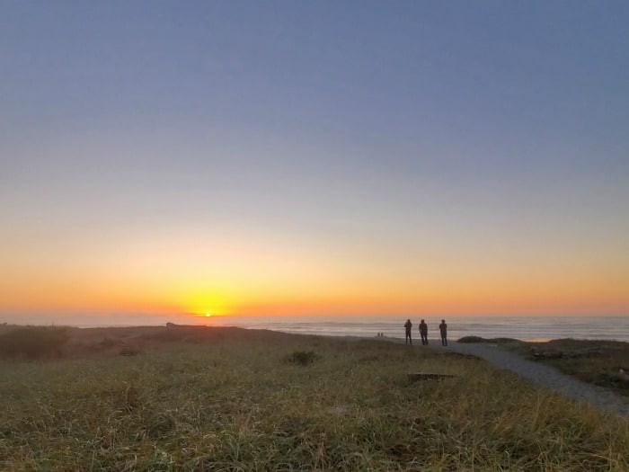 People in the distance on a trail looking out at sunset over the Pacific ocean 