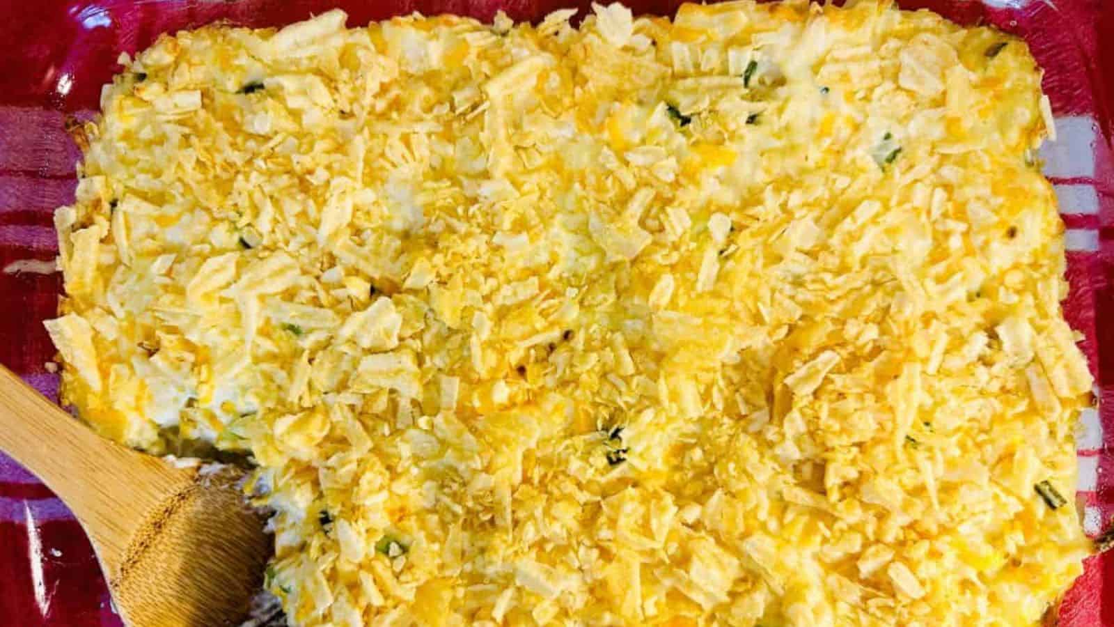 A casserole dish with shredded cheese and a wooden spoon.