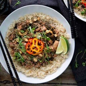 Thai Green Curry topped with peppers and lime wedges on a white plate with black chopsticks on top