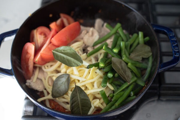 Vegetables are added to Thai red curry paste in a pot.