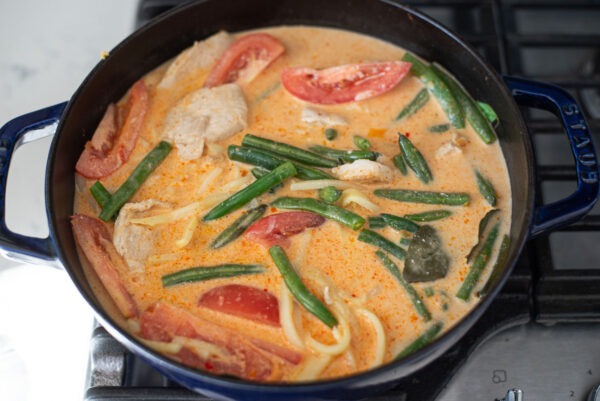 Coconut milk is added to Thai red curry chicken and vegetables in a pot.