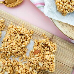 Toasted Coconut Rice Crispy Bars on a light wooden cutting board on a baby pink background