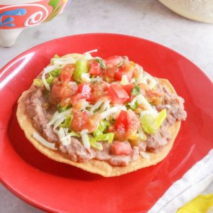 A red plate with a tostada de frijoles (bean tostada)