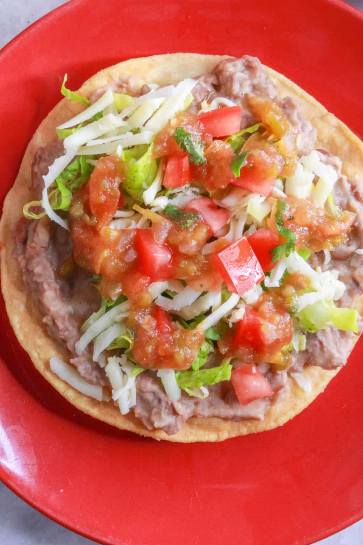 A bean tostada with lettuce, cheese, tomatoes and salsa