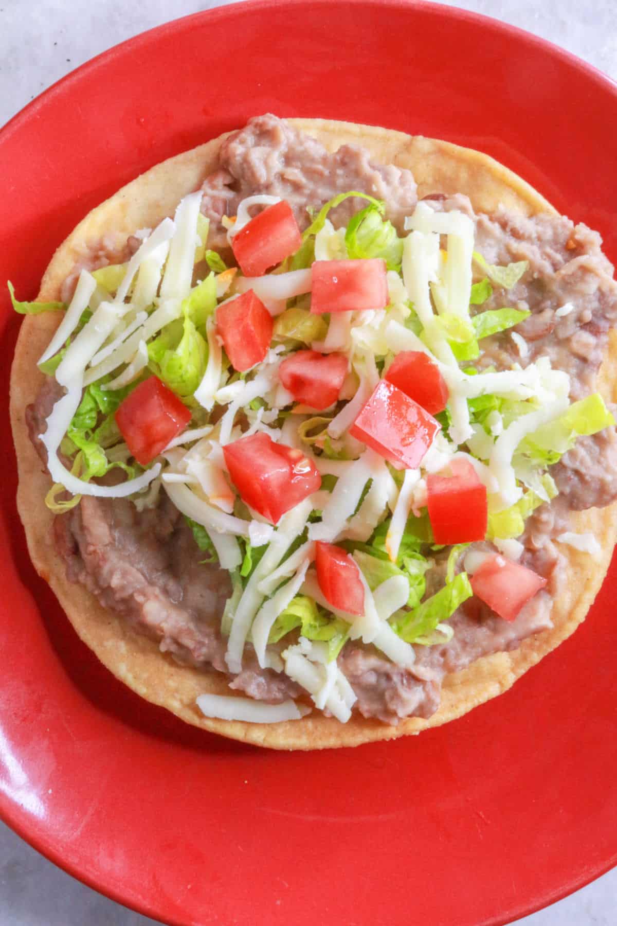 Bean tostada with cheese, lettuce, and tomato