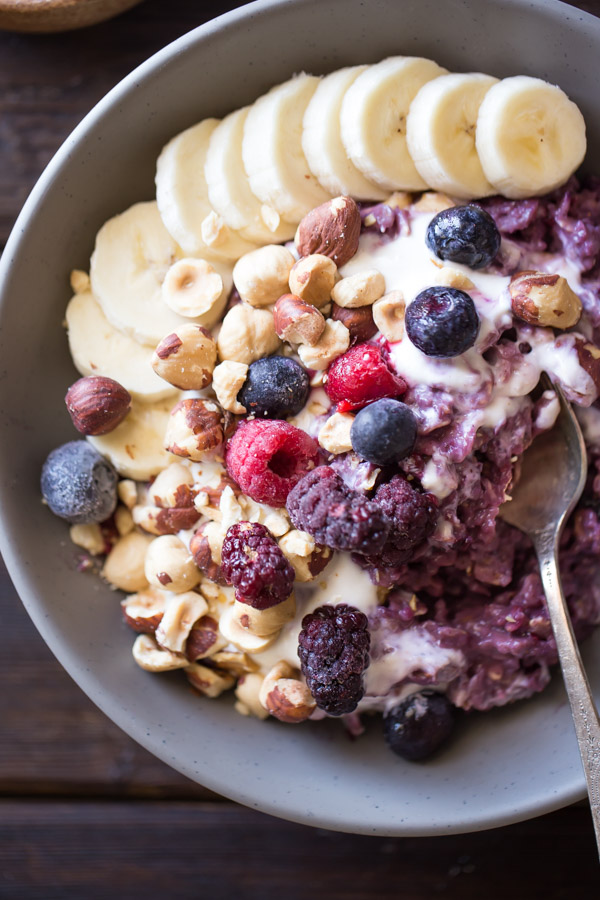 Triple Berry Oatmeal Breakfast Bowl topped with vanilla yogurt, crushed hazelnuts, sliced banana, and berries.