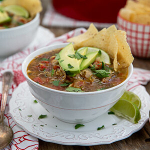 Closeup of Turkey Tortilla Soup in a white bowl on a white plate with red and white placemat