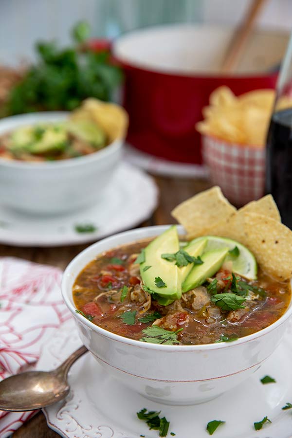 Turkey Tortilla Soup in white bowls with a red soup pot in the background