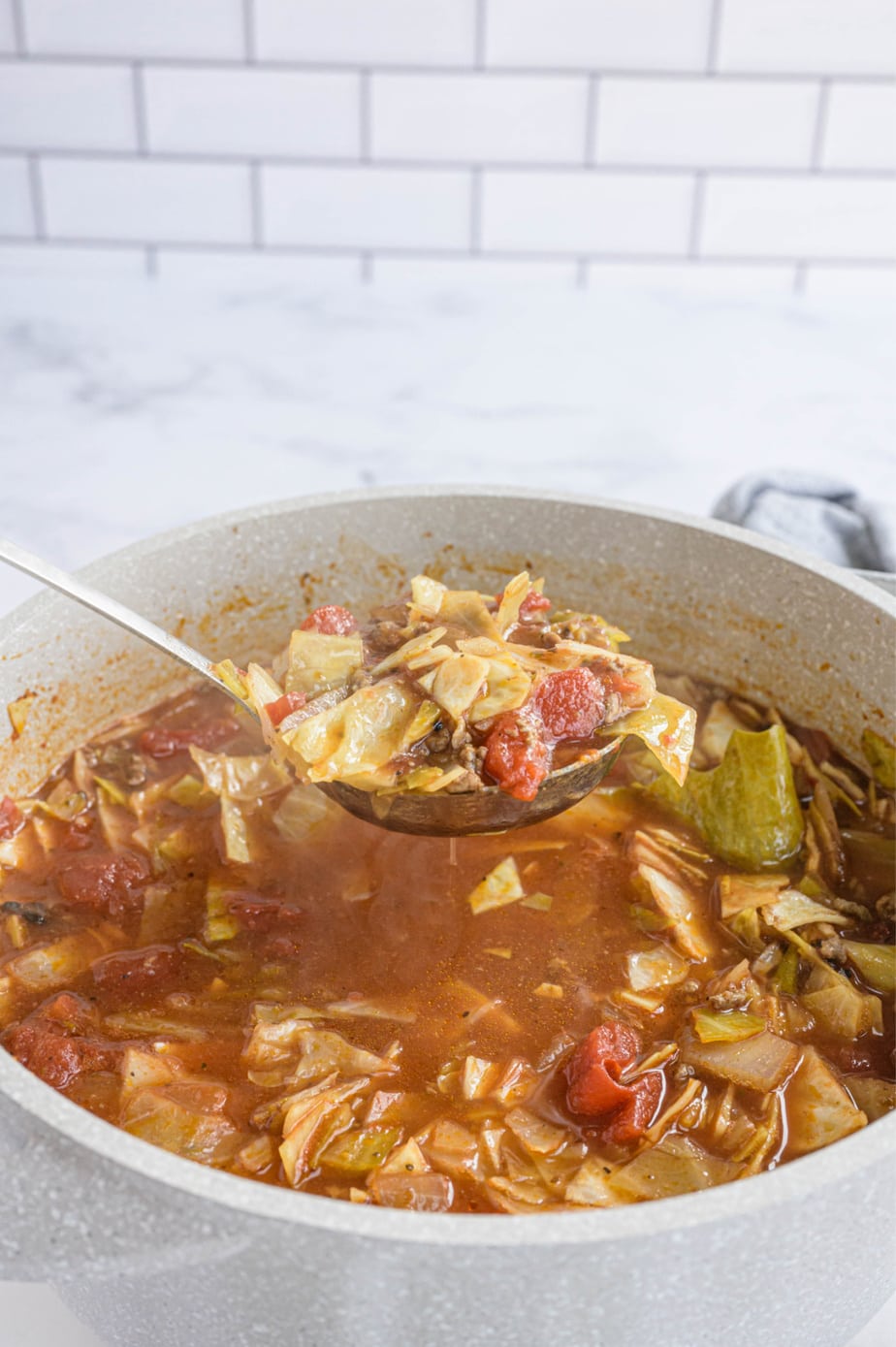 A ladle is holding a large portion of soup over the full pot.