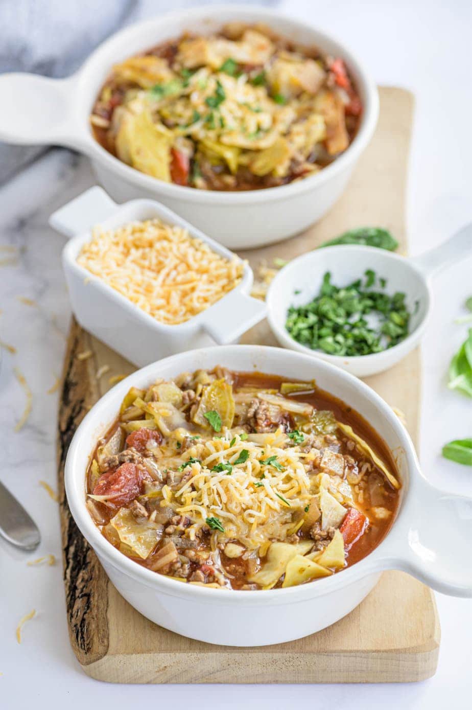 Two bowls of soup are placed next to small bowls of cheese and parsley.