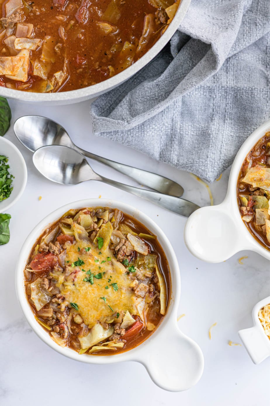 Two white bowls filled with soup are on a white surface. 