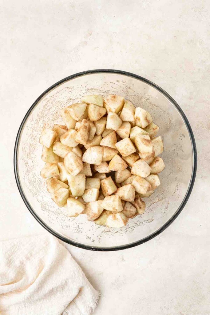 Chopped apples tossed with cinnamon and sugar in a glass mixing bowl.