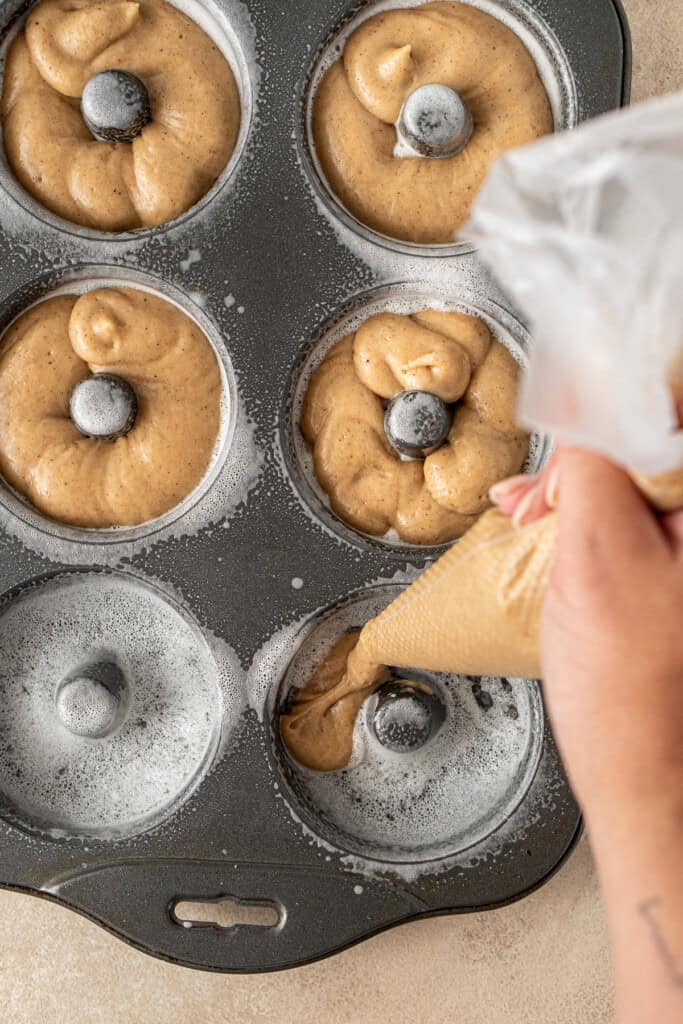 Using a piping bag to add the filling to the doughnut pan.