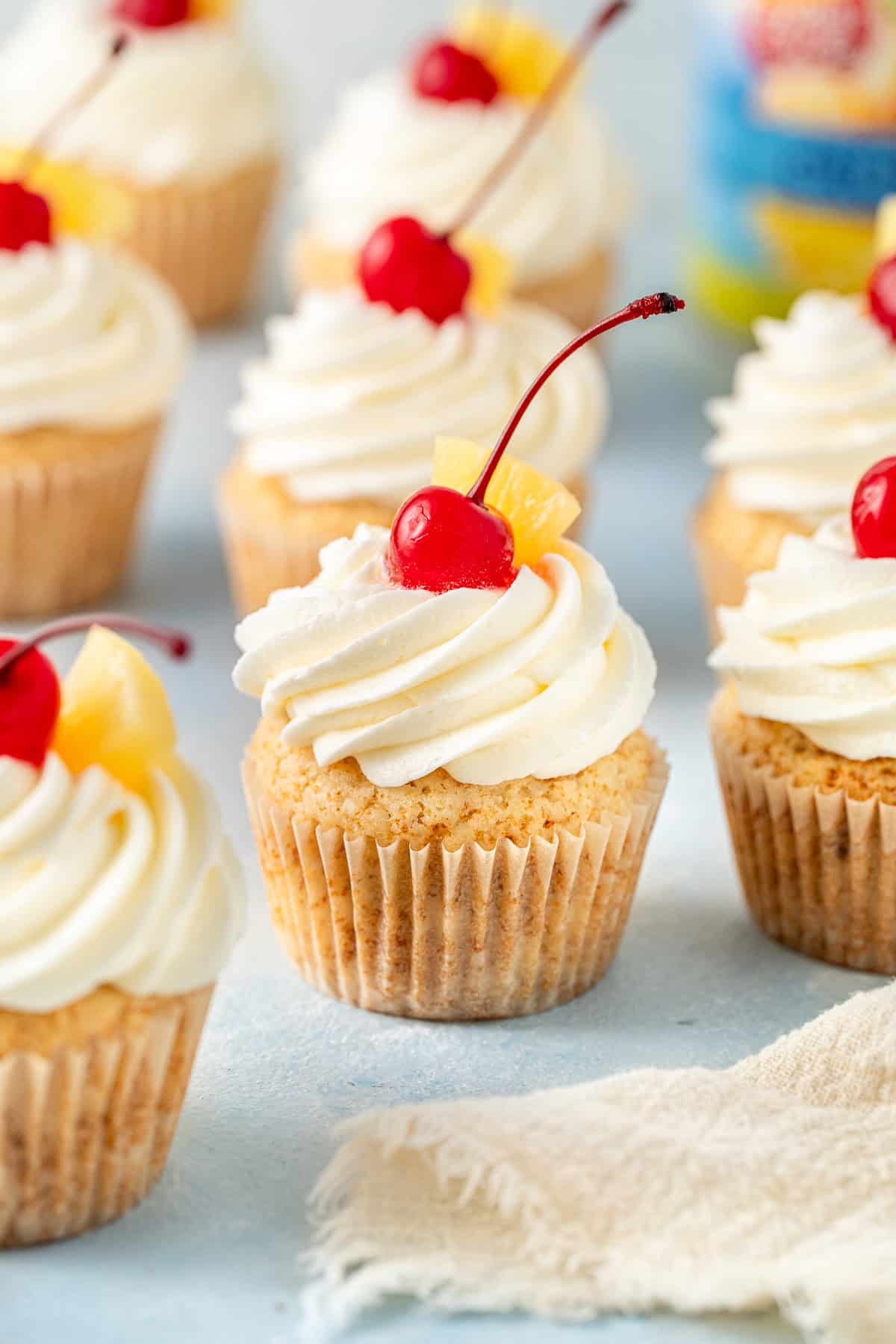 Vegan pineapple cupcakes with pineapple buttercream and topped with a cherry.