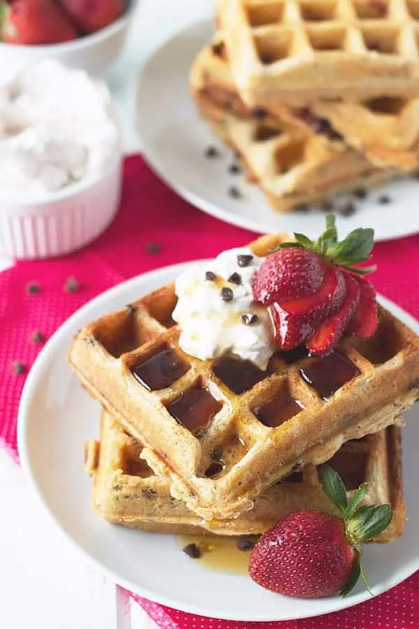 2 waffles with strawberries, syrup, whipped cream, chocolate chips, and fresh berries on top