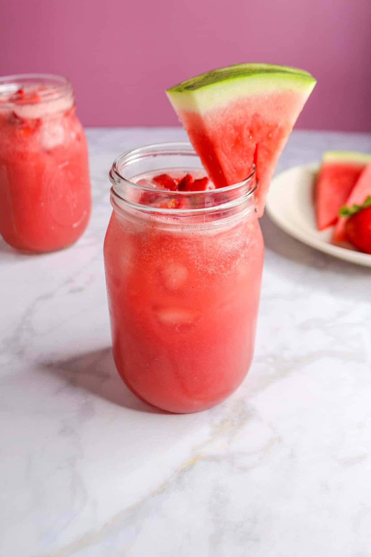 Watermelon Strawberry Agua Fresca in a glass garnished with a slice of watermelon, another full glass behind it