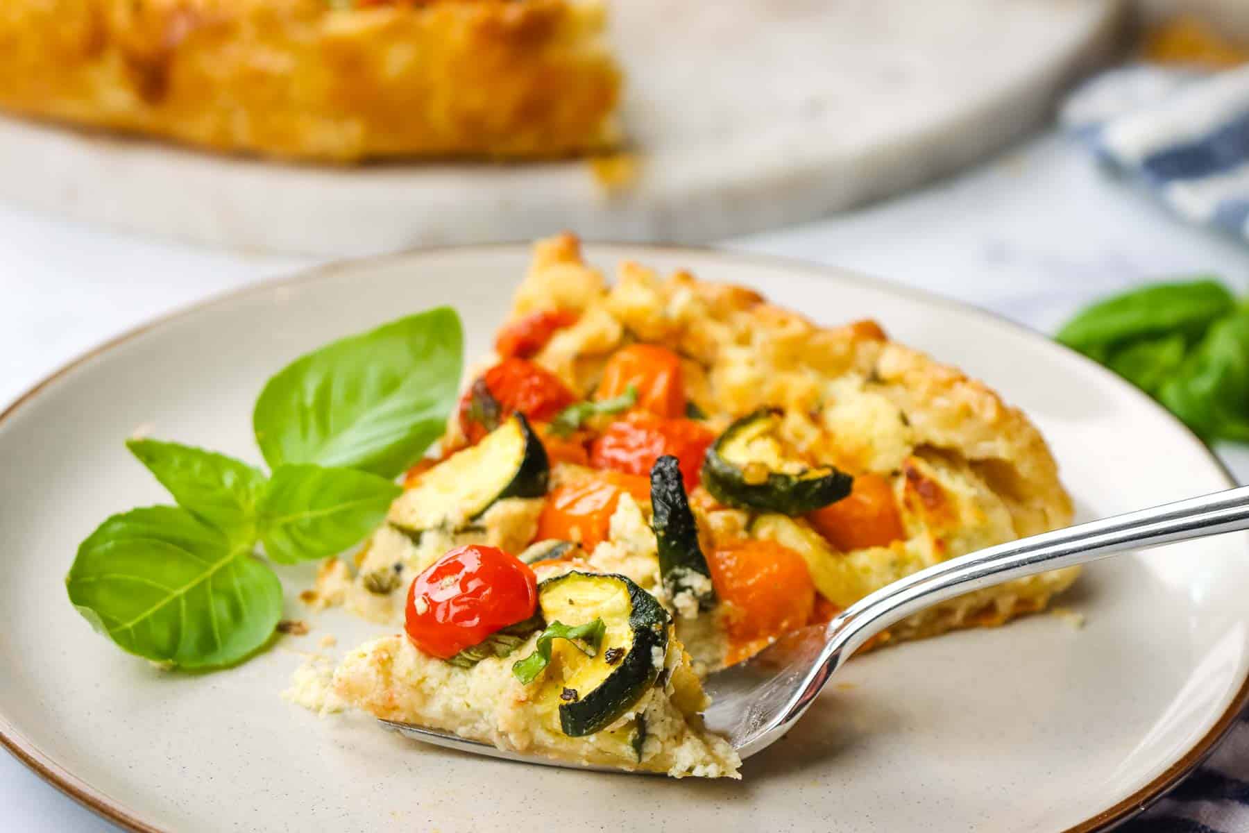 cutting into a slice of zucchini tomato tart with a fork