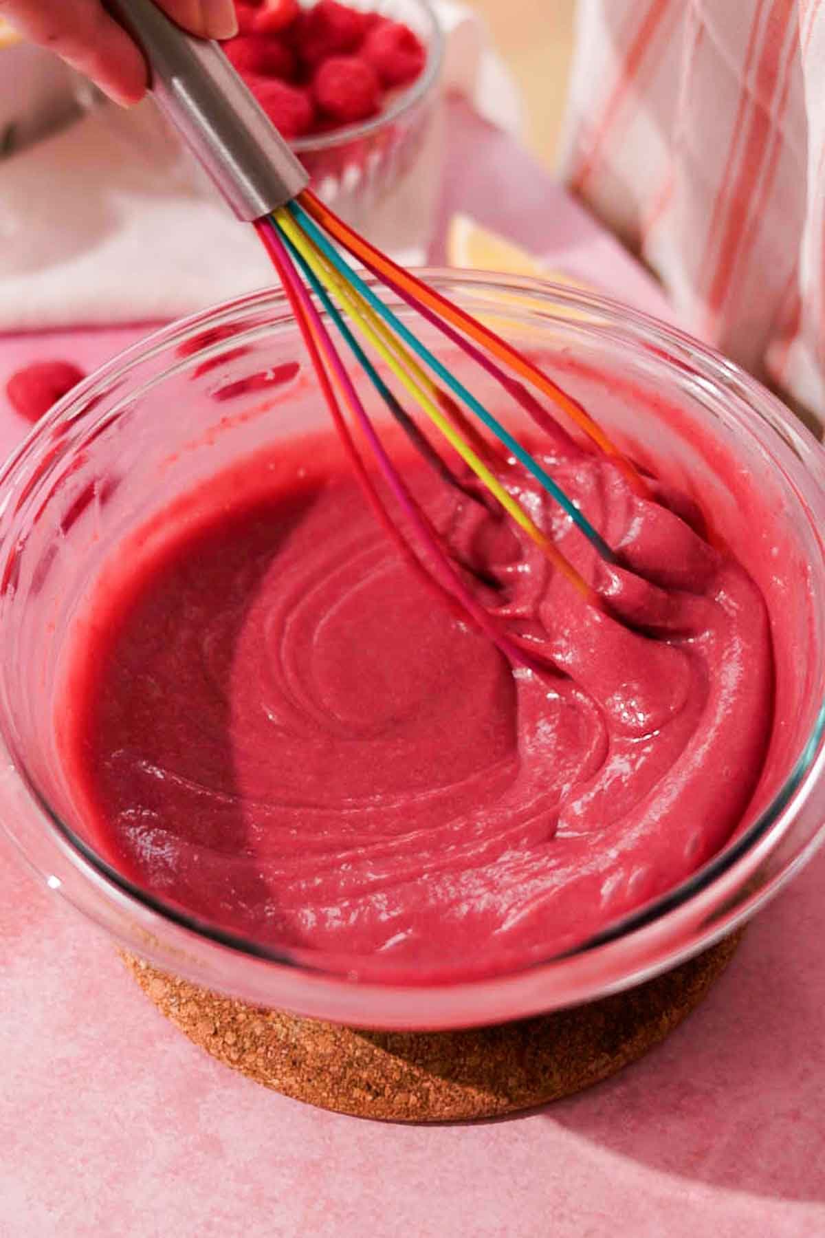 whisking raspberry curd in large bowl with silicone whisk