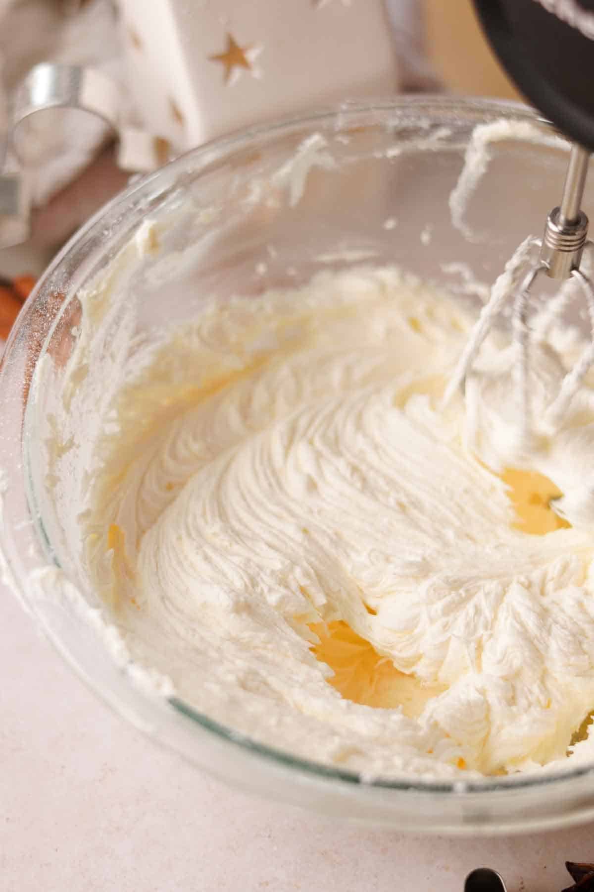 beating frosting for cupcakes in a glass bowl with an electric mixer