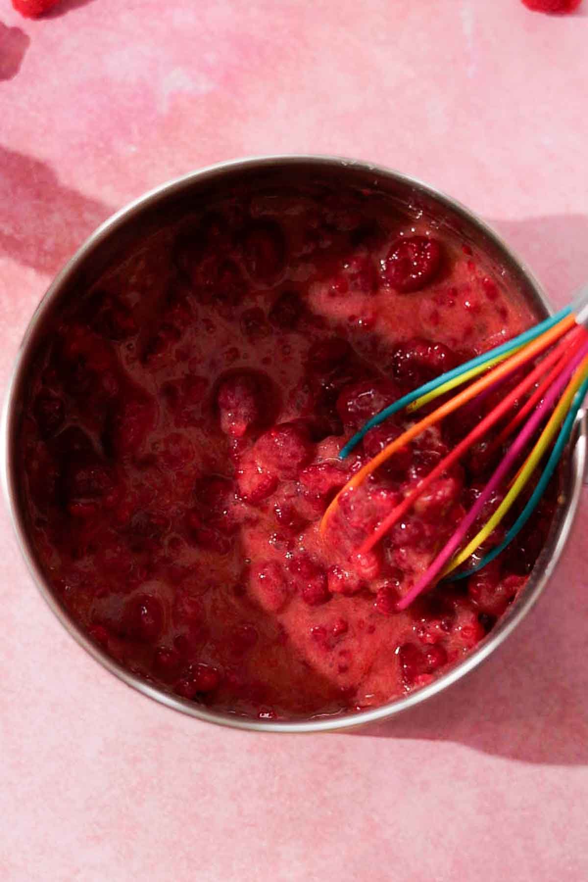 stirring uncooked raspberry curd with a silicone whisk in metal saucepan