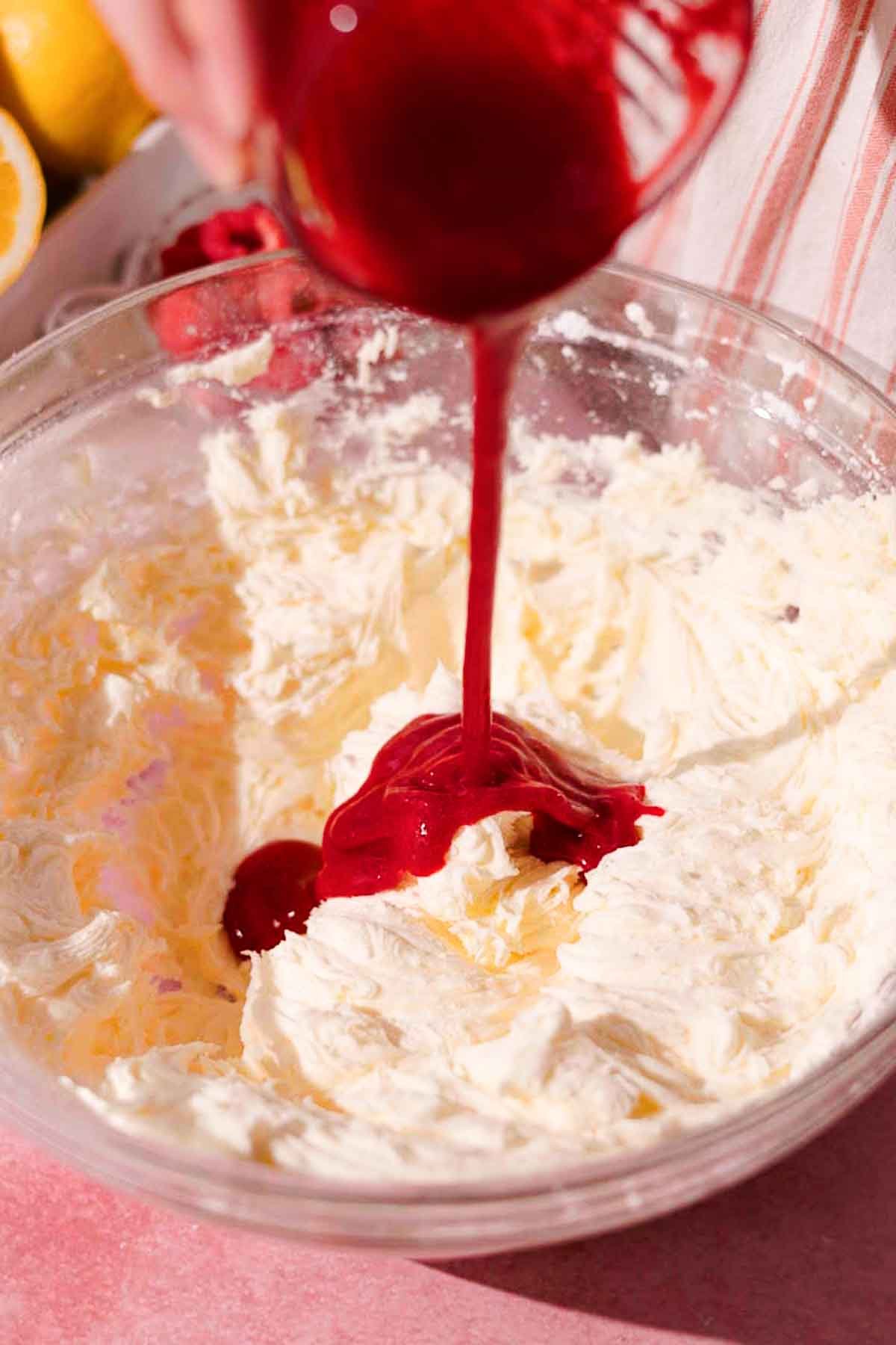 adding raspberry puree to frosting in large glass bowl