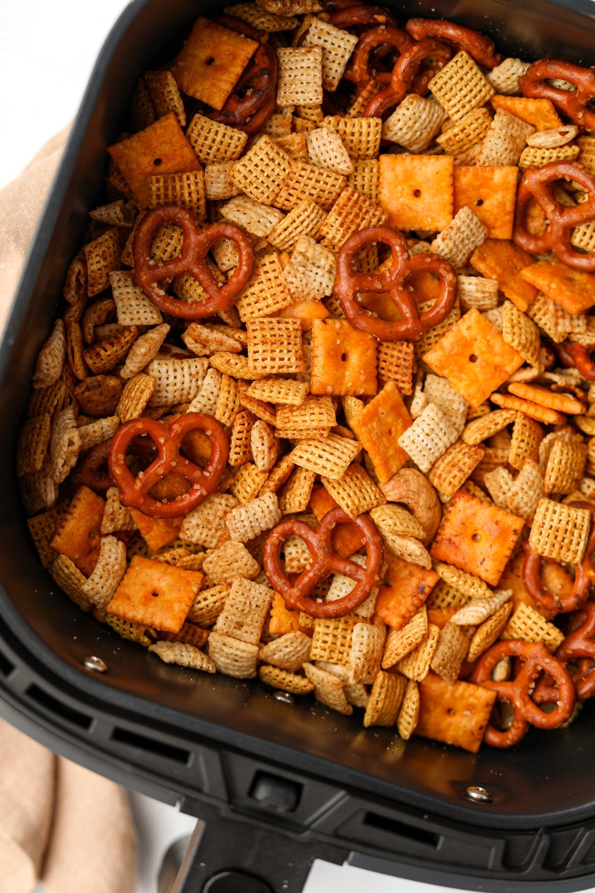 An air fryer basket filled with snack mix featuring pretzels, cereal, and cheez-its.