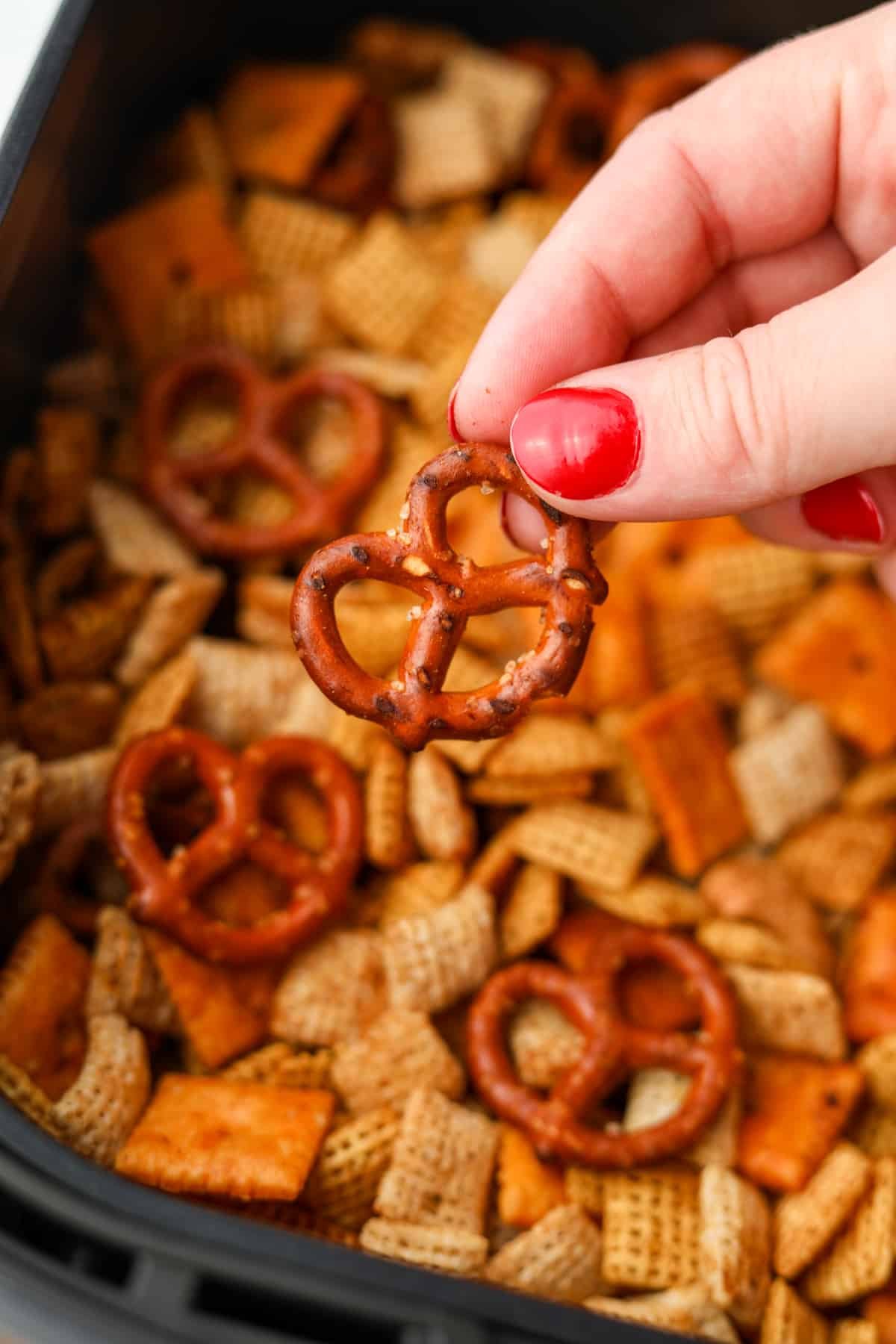 A hand lifting a pretzel from a homemade snack mix.