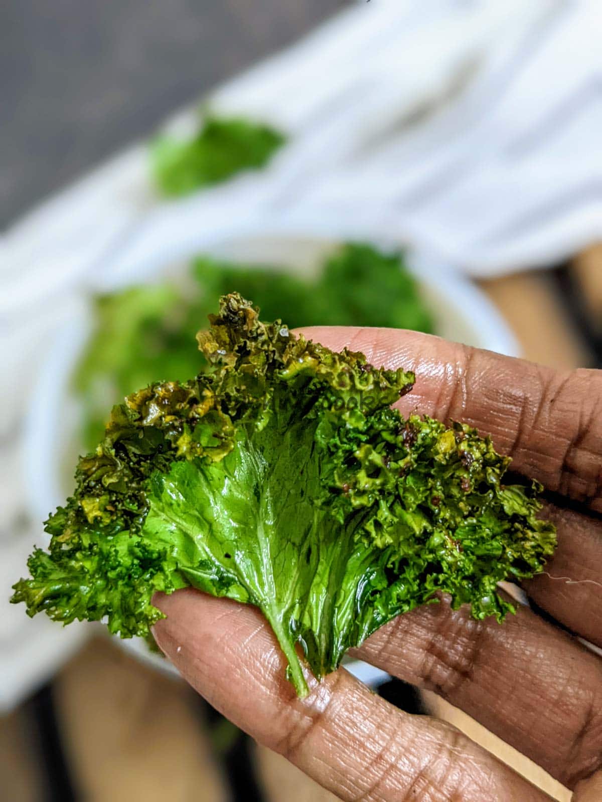 Close up of one kale chips after air frying in a white bowl.