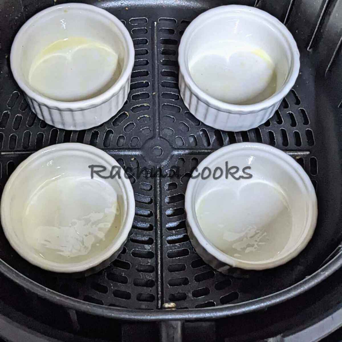 4 ramekins brushed with oil in air fryer basket after preheating.