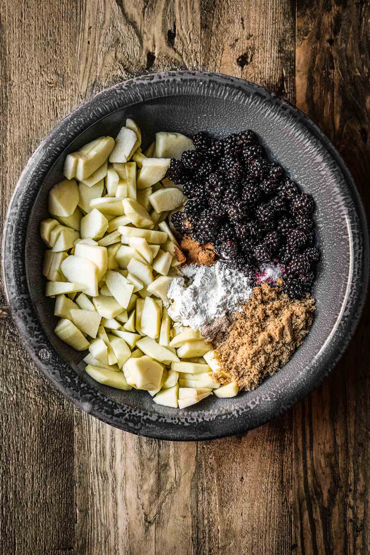 A bowl of chopped apples, blackberries, sugar and spices before mixing. 