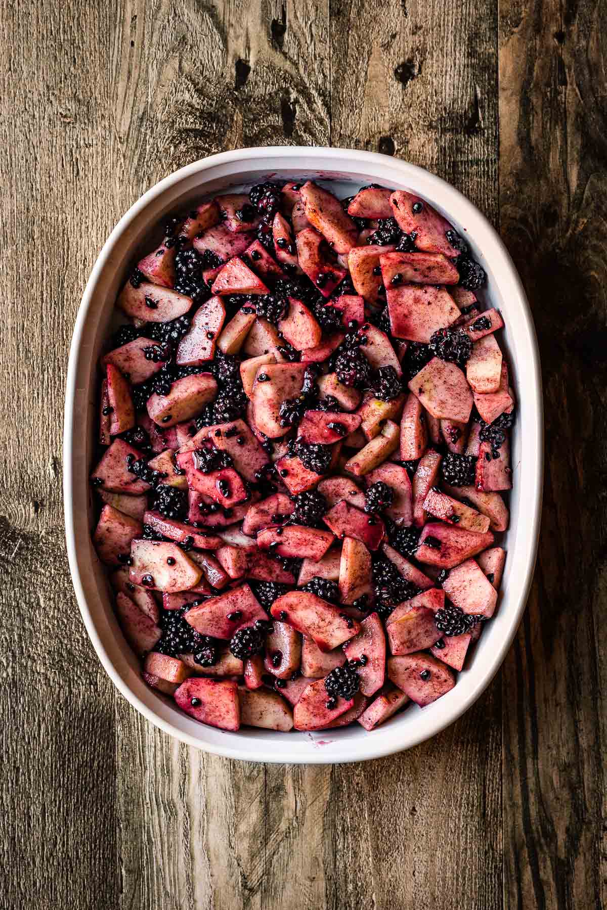 A baking dish filled with uncooked peeled, chopped apples and blackberries.