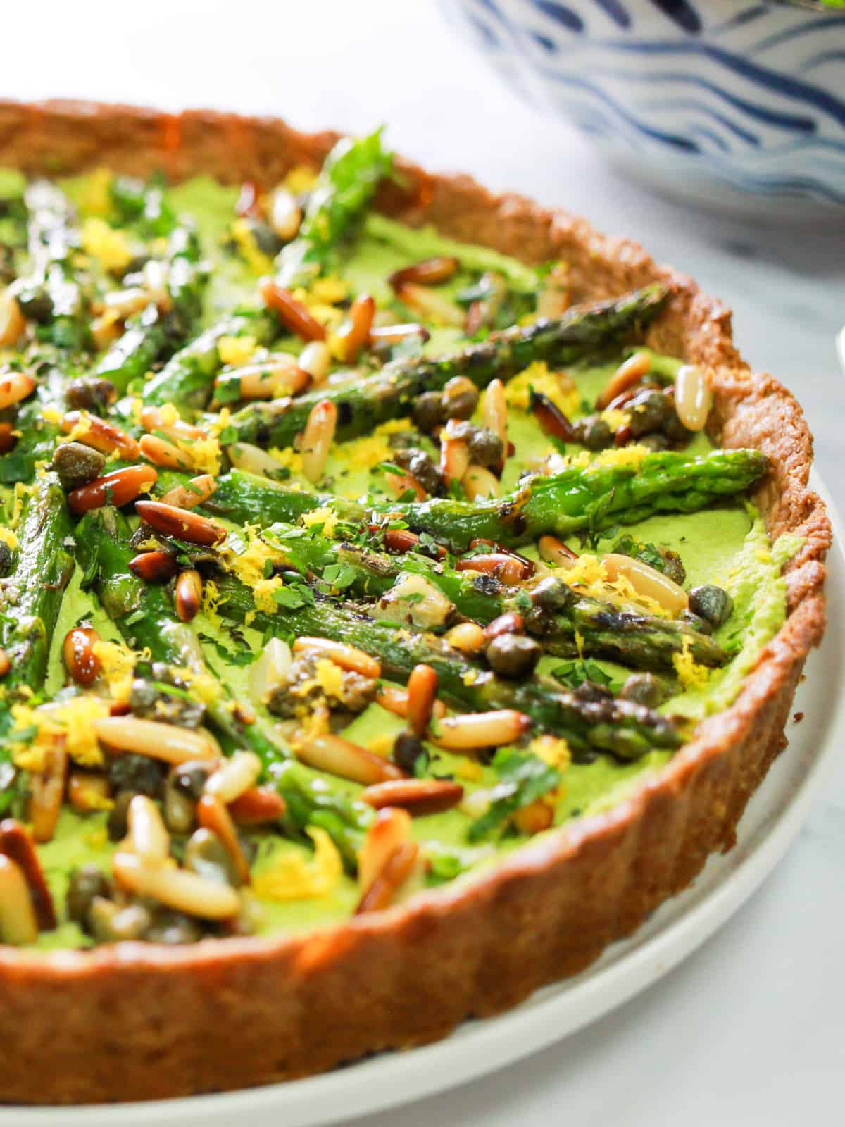 close-up photo of half of a whole vegan asparagus tart with pesto macadamia filling.