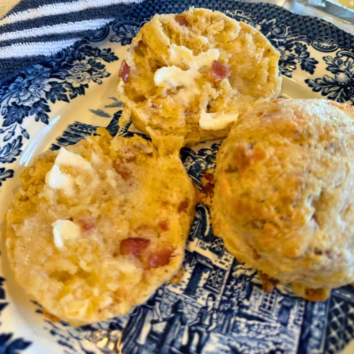 bacon cheddar sourdough biscuits on a blue plate. One is sliced with butter on it and one is whole.