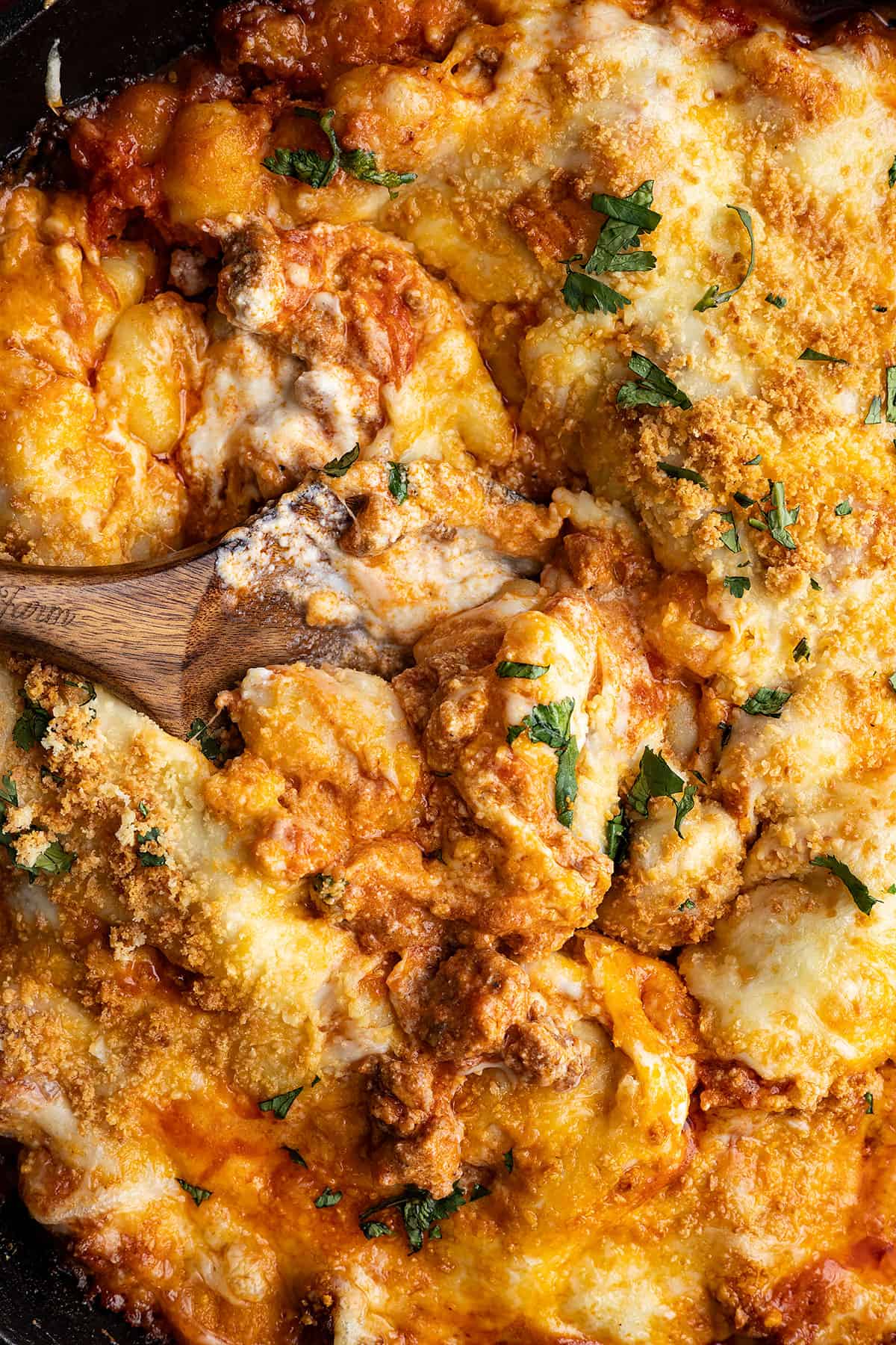 Overhead view of baked gnocchi with a spoon in the middle showing how gooey the casserole is.