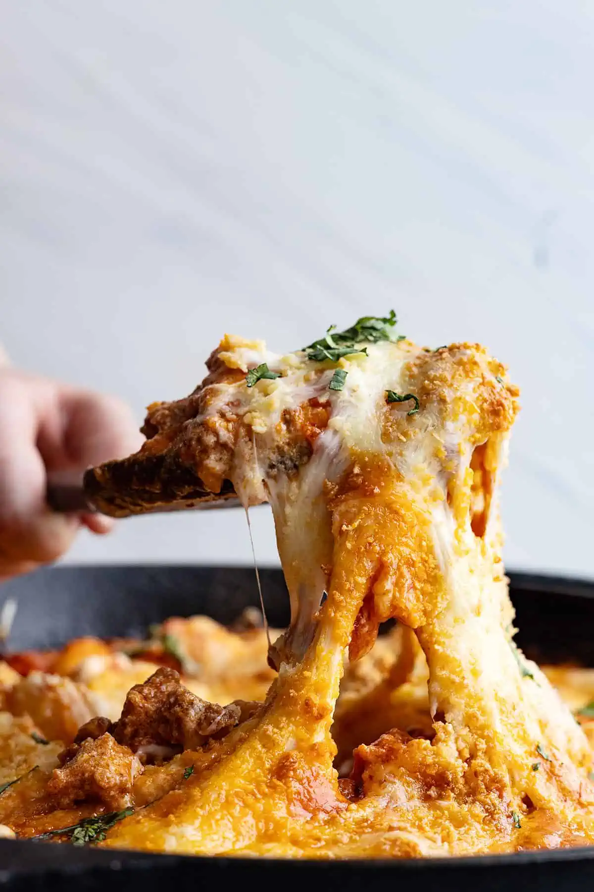 Spoon pulling up a cheese pull full of cheesy gnocchi.