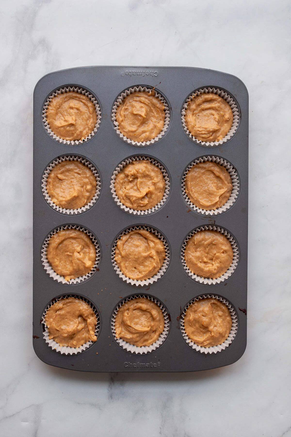 Banana pumpkin muffin batter scooped into paper liners in a muffin tin, ready to bake.