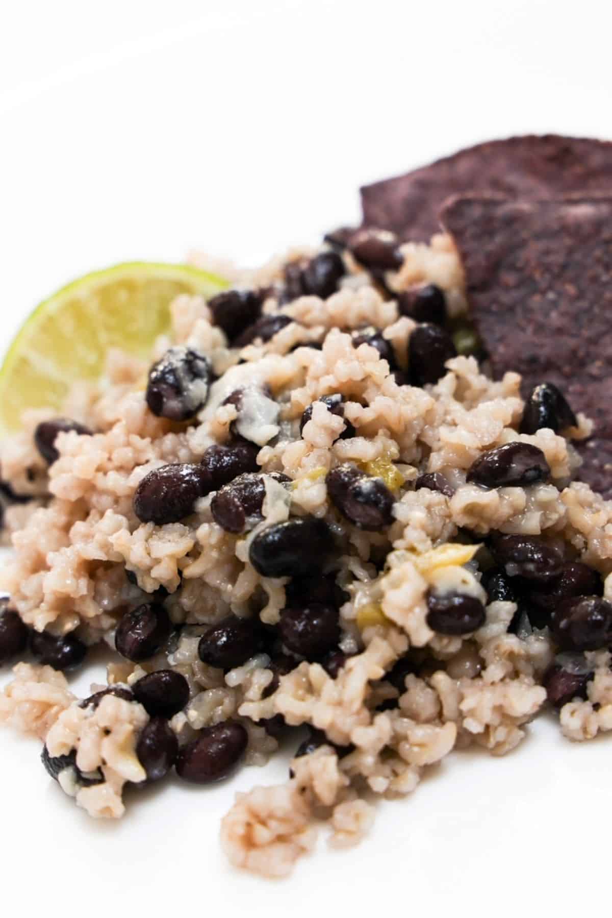 Black beans and rice with a lime wedge and a few blue tortilla chips on a white plate.