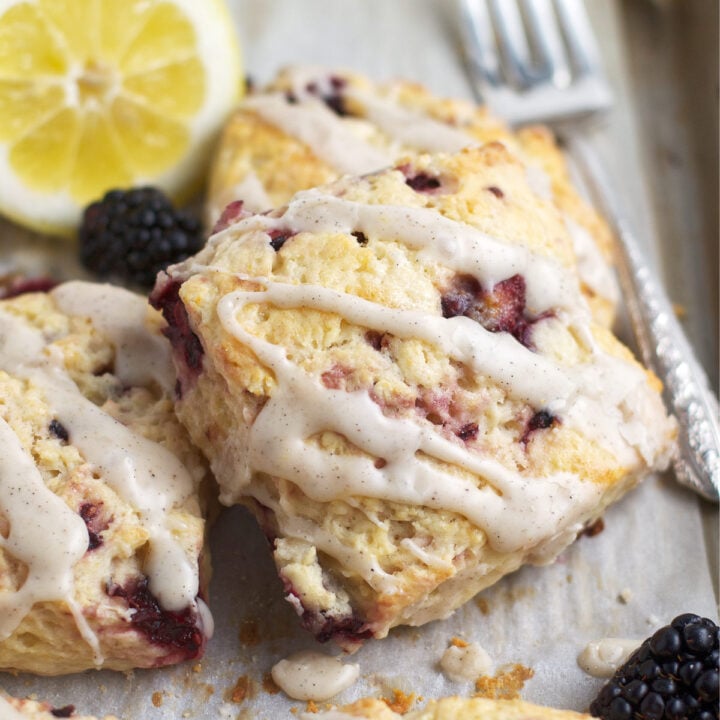 blackberry lemon scone with fresh lemon glaze on a baking sheet with lemons and blackberries