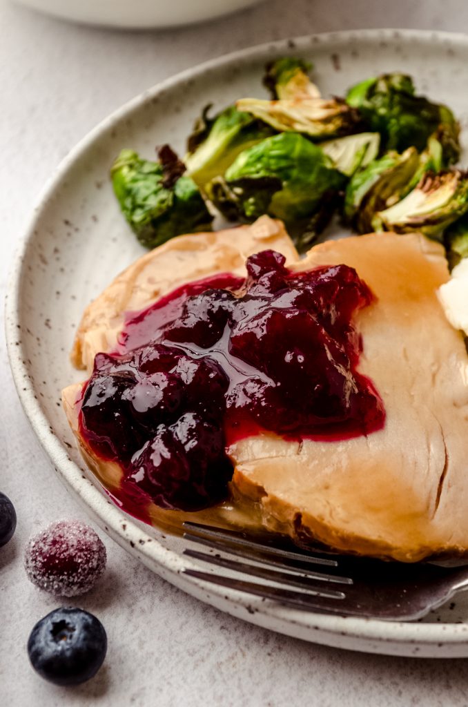 Blueberry cranberry sauce on slices of turkey on a plate with Brussels sprouts and a fork.