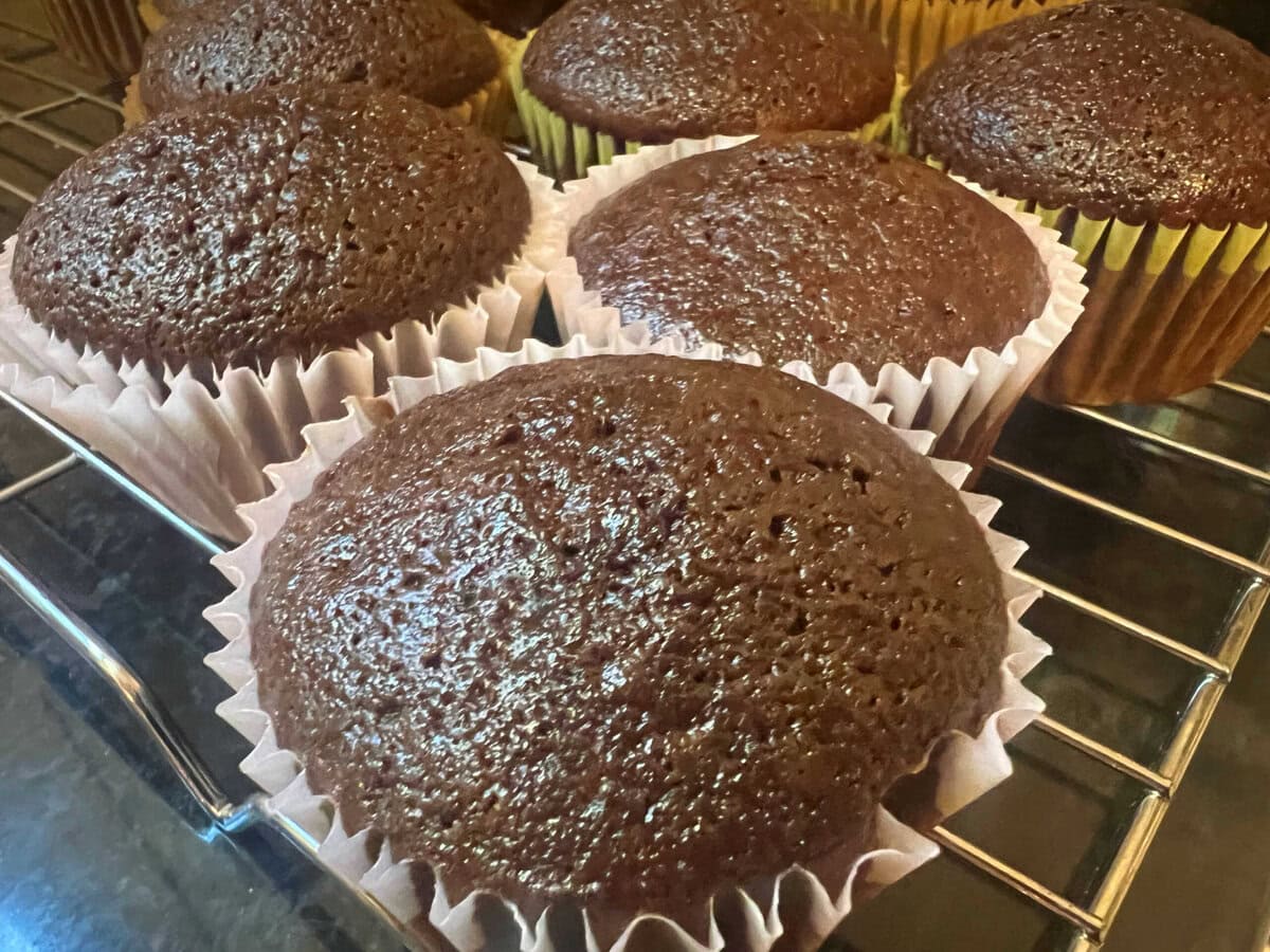 Unfrosted, freshly baked cupcakes cooling on a wire rack.
