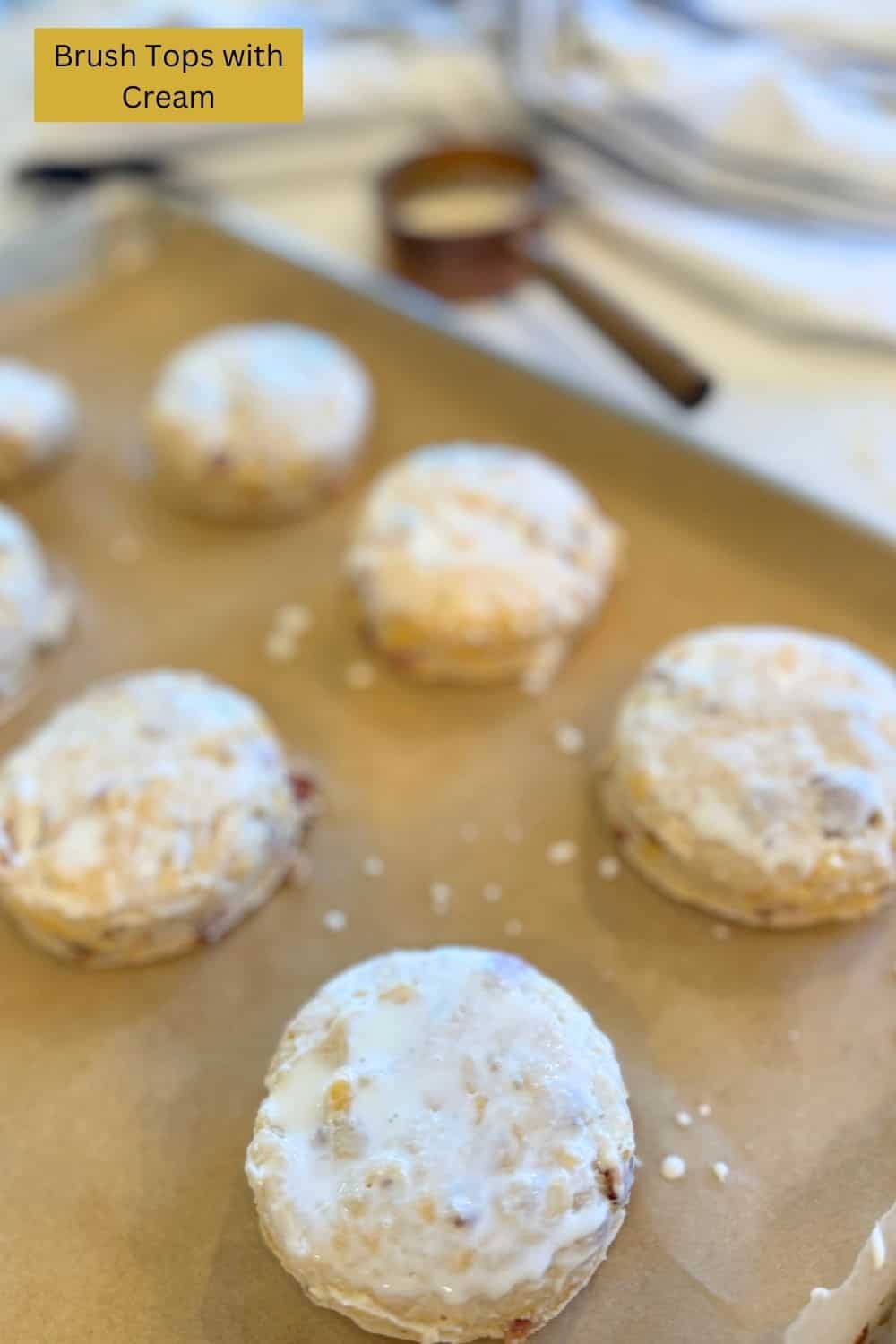 raw bacon cheddar sourdough biscuits with tops that have been brushed with cream on a parchment lined baking sheet