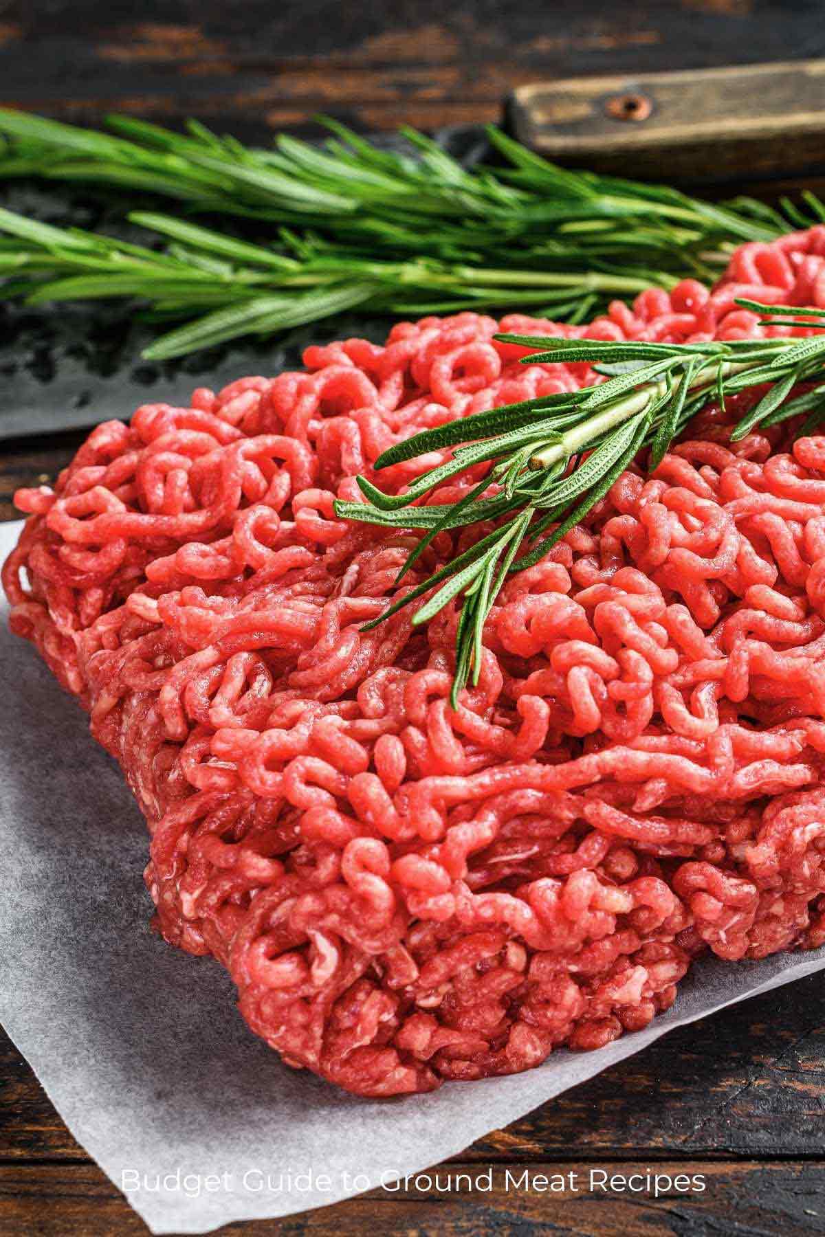 Ground beef, fresh rosemary, and sage on a butcher's block for delicious ground meat recipes.