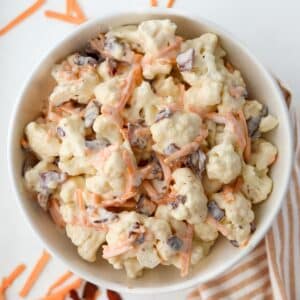 A bowl of cauliflower salad dotted with cheese and bacon.