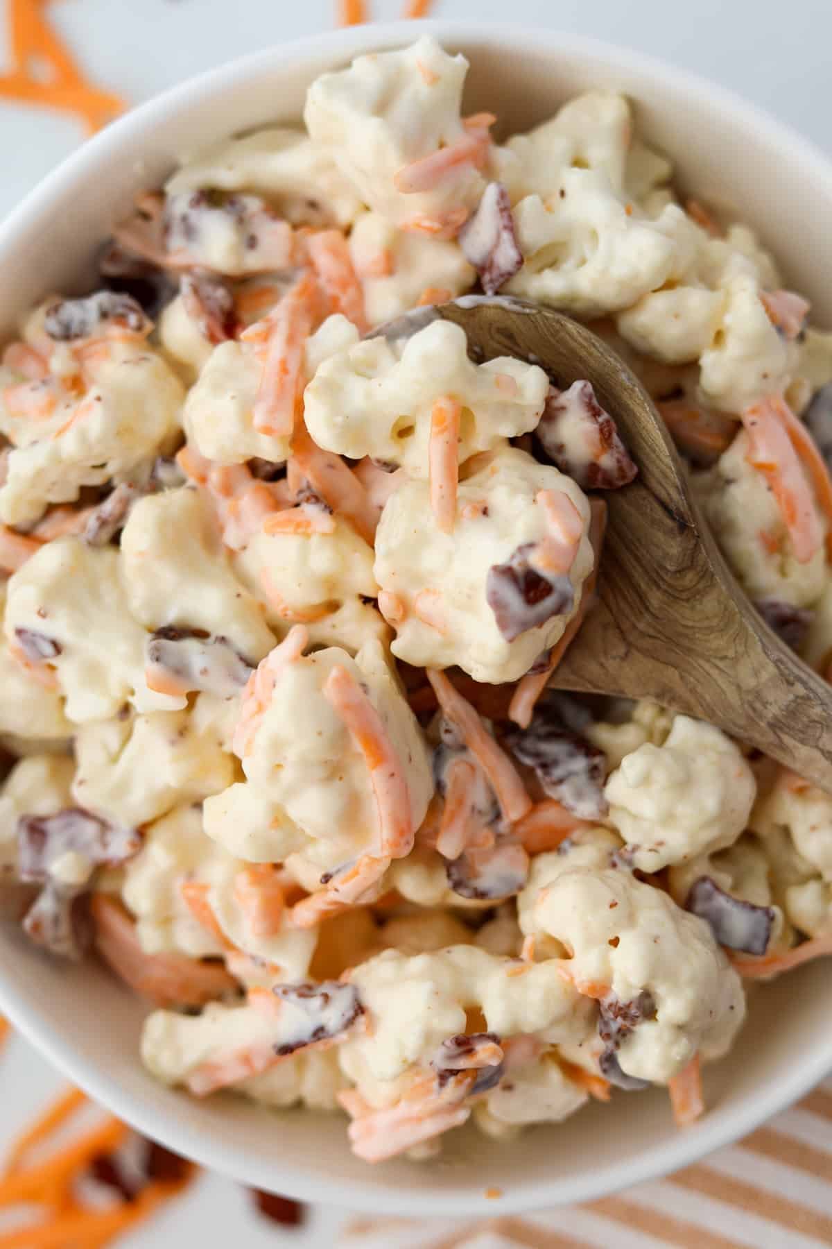 A wooden spoon holding several cauliflower florets covered in a creamy dressing.