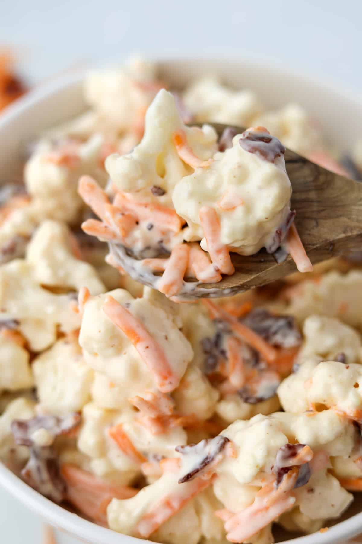 A wooden spoon lifting cauliflower salad from a bowl.