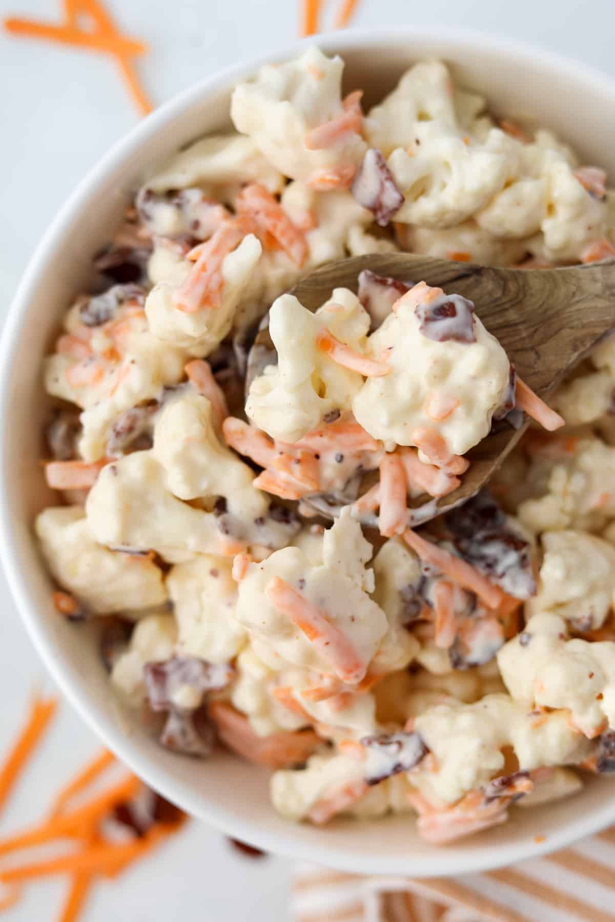 A wooden spoon scooping some cauliflower salad from a bowl.