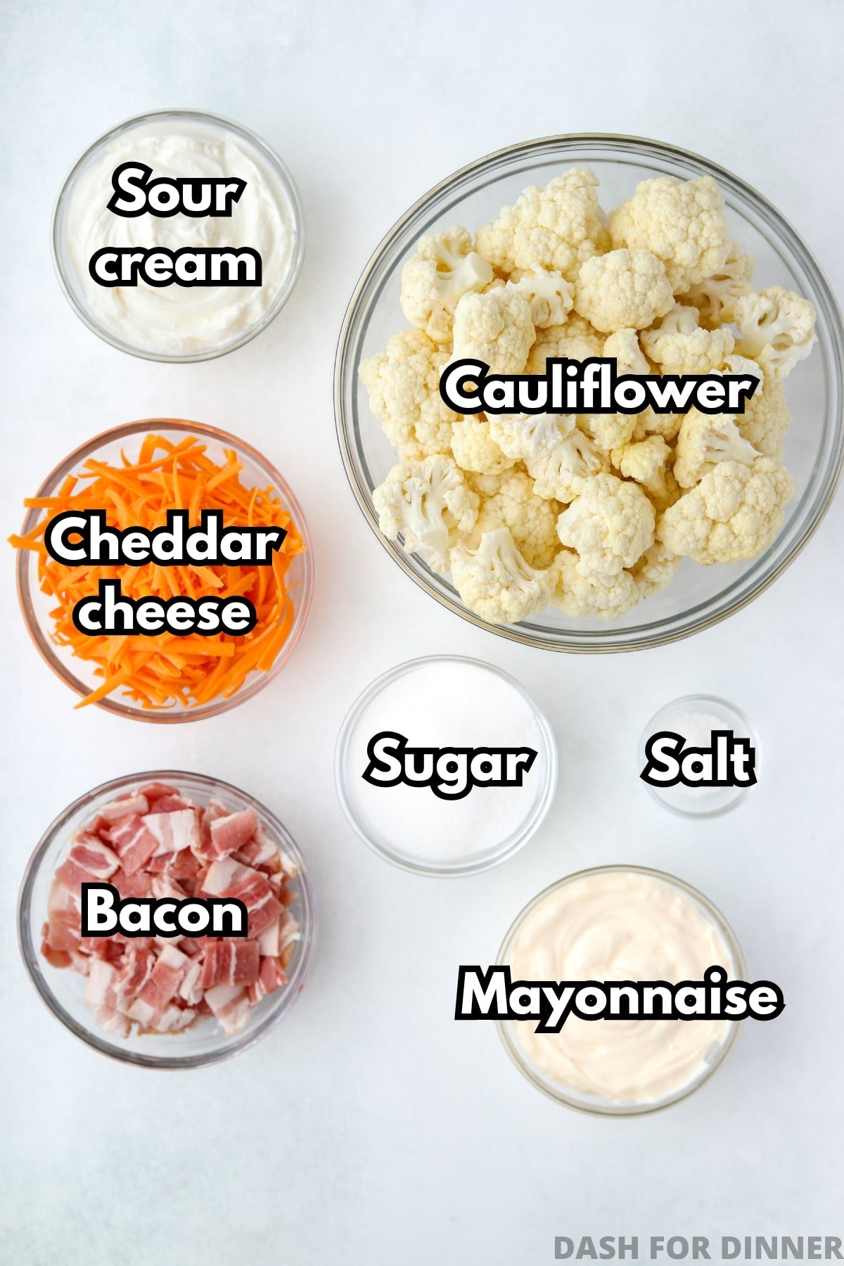 The ingredients needed to make cauliflower salad: cheese, sour cream, mayonnaise, bacon, and cauliflower florets.