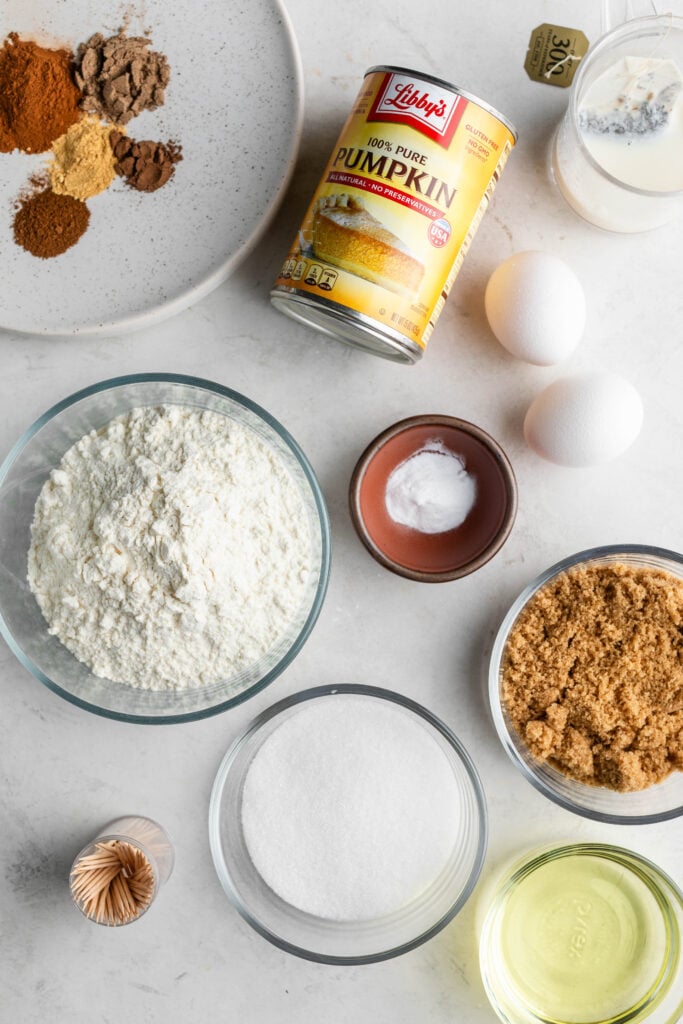 chai latte pumpkin spice bread ingredients. plate with spices on it, 1 can of libbys 100% pure pumpkin, 2 eggs, a bowl of flour, brown sugar, granulated sugar, oil, chai tea, and baking soda. 